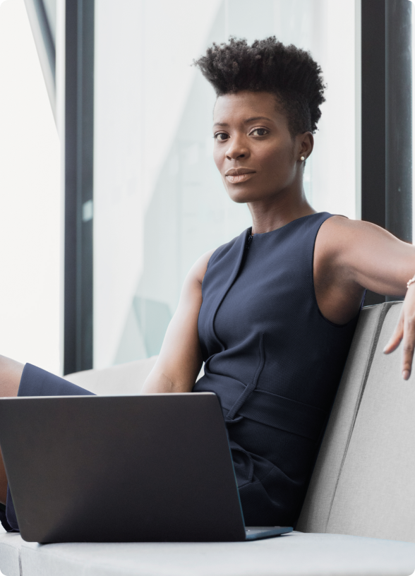 Mulher de vestido azul marinho sentada com notebook, olhando para a câmera com confiança.