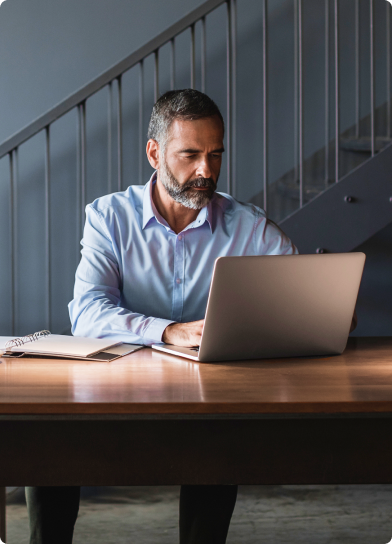 Homem de barba grisalha trabalha no notebook em um ambiente sofisticado.