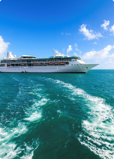 Navio de cruzeiro em mar azul com céu limpo e rastro de água ao fundo.