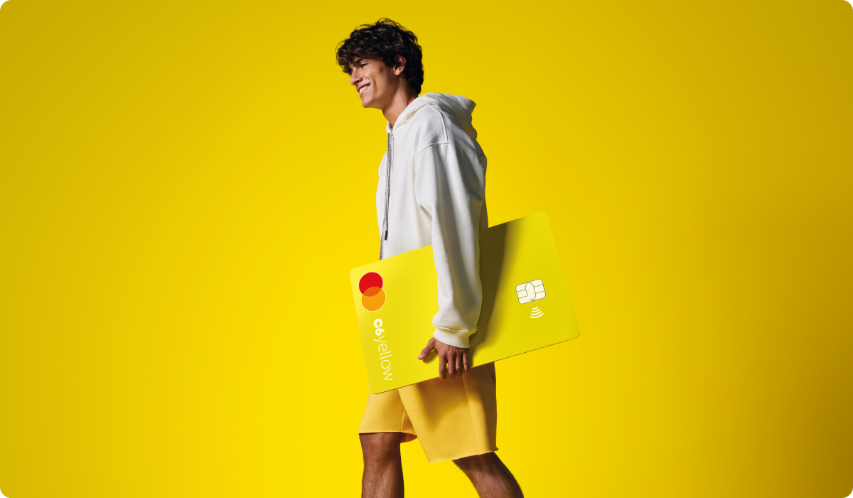Menino sorri enquanto caminha segurando cartão C6 Yellow ampliado. Fundo e roupas seguem tom amarelo vibrante.