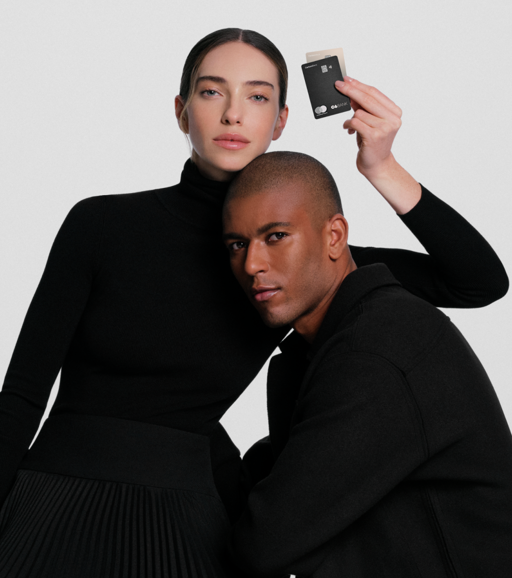 Casal elegante veste preto; a mulher segura dois cartões do C6 Bank, destacando exclusividade e sofisticação.