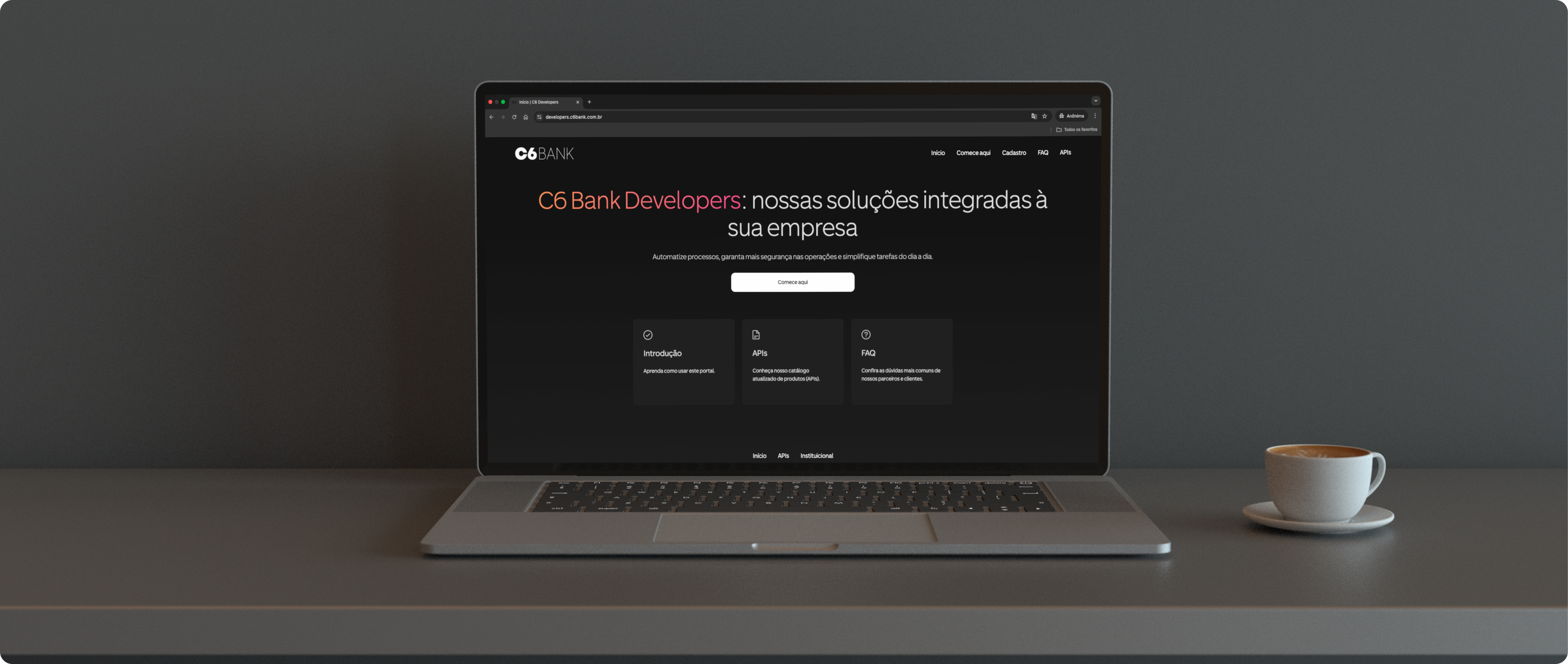 Laptop com a página do C6 Bank Developers ao lado de uma xícara de café.