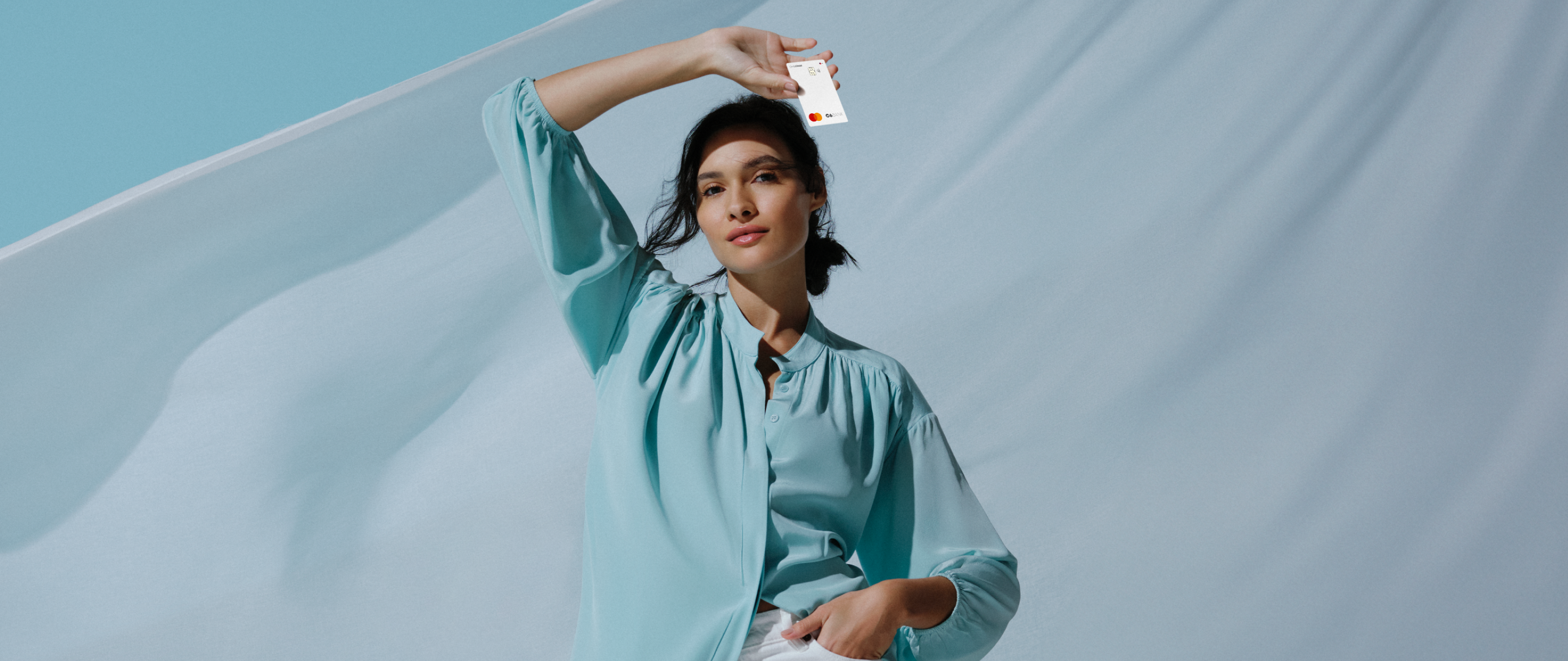 Mulher de blusa azul segura um Cartão C6 Mastercard acima da cabeça.