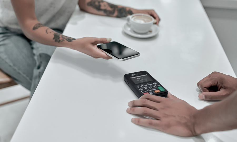 Pagamento por aproximação sendo feito em uma maquininha C6 Pay sobre uma mesa branca.