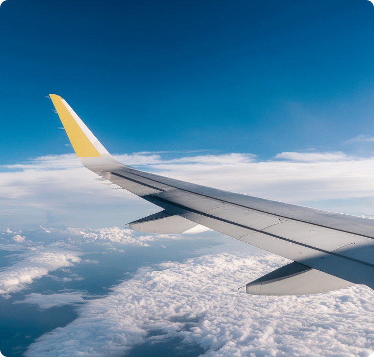 Asa de avião em voo, com céu azul e nuvens abaixo.