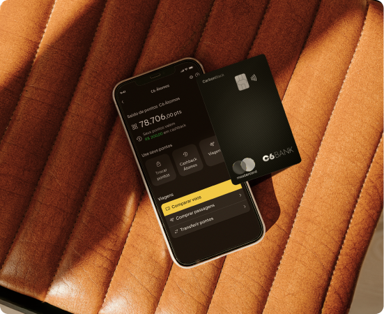 Celular com app do C6 Bank e cartão C6 Carbon Mastercard Black sobre assento caramelo, exibindo troca de pontos por dinheiro.
