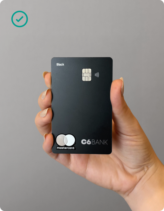 Mão feminina segurando o cartão do C6 Bank na lateral e no meio de sua mão.