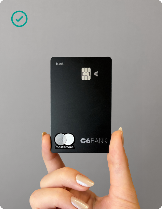 Mão feminina segurando o cartão do C6 Bank pela parte inferir, no formato de pinça.