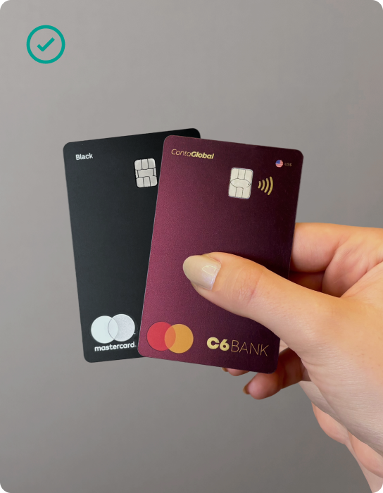 Mão feminina segurando dois cartões do C6 Bank, de forma a exibir a categoria e logo da Mastercard em ambos.