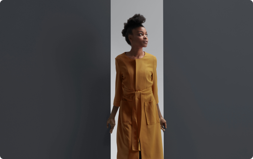 Mulher de vestido mostarda caminha entre duas paredes escuras.