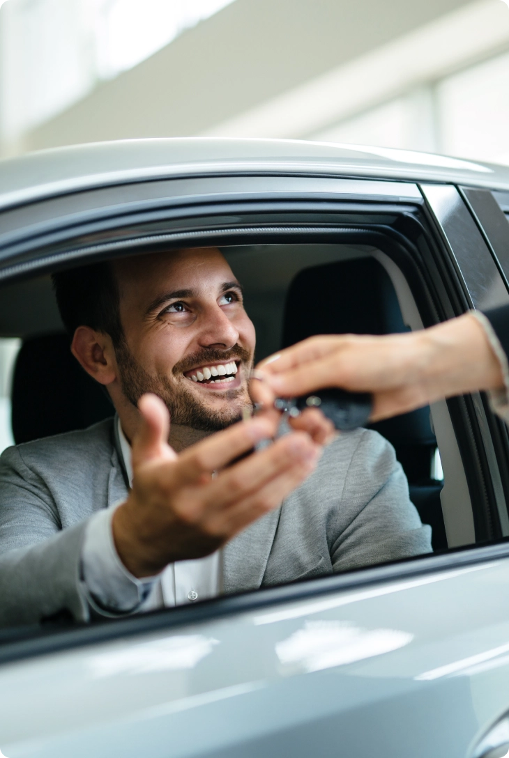 Homem dentro de um carro recebe uma chave pela janela e sorri.