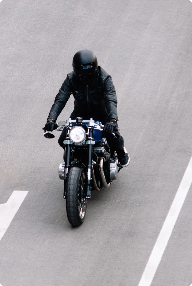 Motociclista de preto conduz uma moto em via asfaltada, visto de cima.