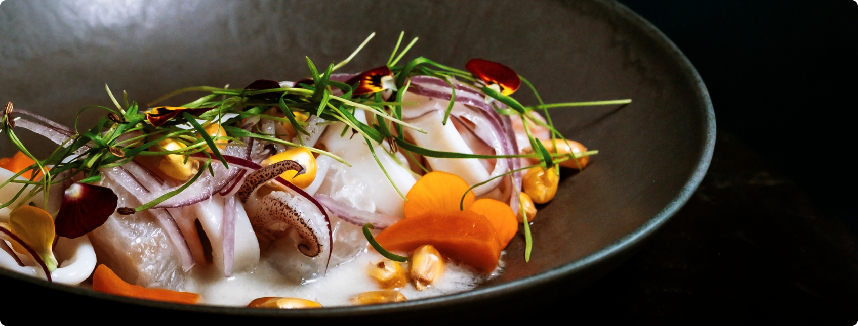 Prato gourmet com frutos do mar, cebola roxa, flores e brotos sobre molho cremoso.