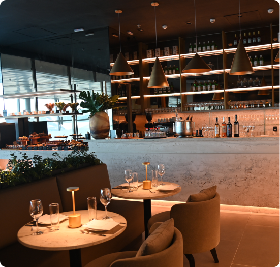 Restaurante da Sala Vip The Club com mesas montadas, balcão de mármore e prateleiras iluminadas com garrafas e taças.