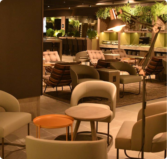 Sala VIP elegante com poltronas, mesas baixas, iluminação suave e área de buffet ao fundo.