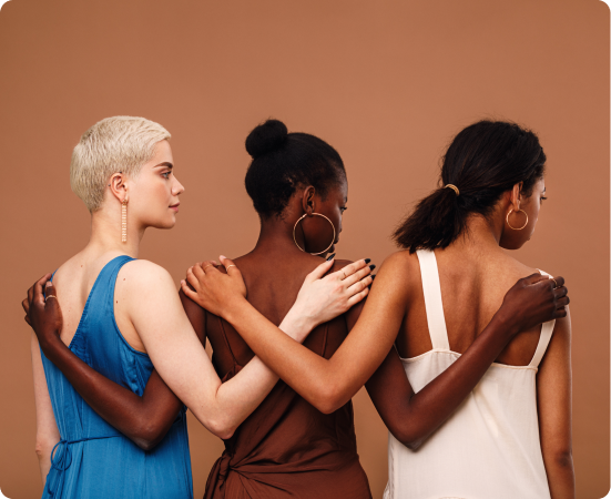 Fotografia de 3 mulheres de costas se abraçando, com suas cores de pele em contraste.