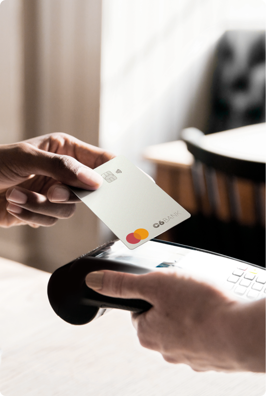Cartão C6 Bank sendo usado em pagamento por aproximação em maquininha.