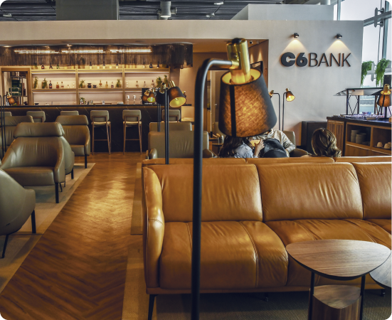 Sala VIP do C6 Bank com sofás de couro, buffet e logo da marca na parede em ambiente sofisticado.