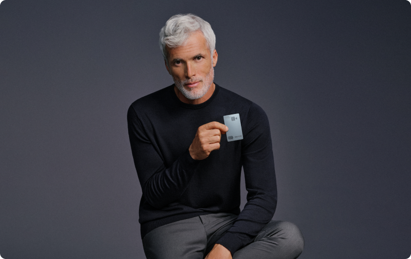 Homem segura o Cartão C6 Graphene com fundo neutro; visual sofisticado e elegante.