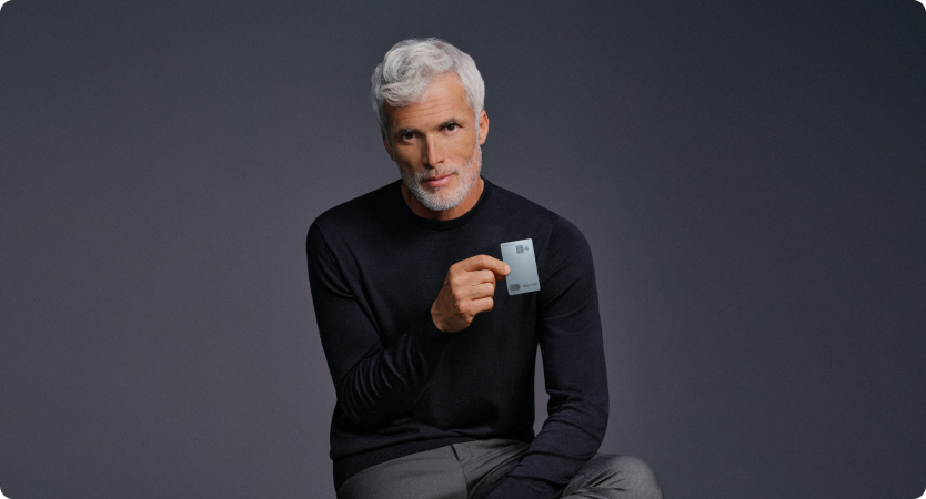 Homem segura o Cartão C6 Graphene com fundo neutro; visual sofisticado e elegante.