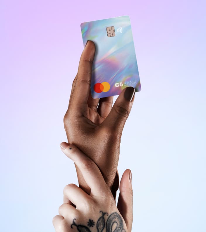 Duas mãos entrelaçadas, uma segurando um Cartão C6 Bank holográfico, contra um fundo lilás e azul.