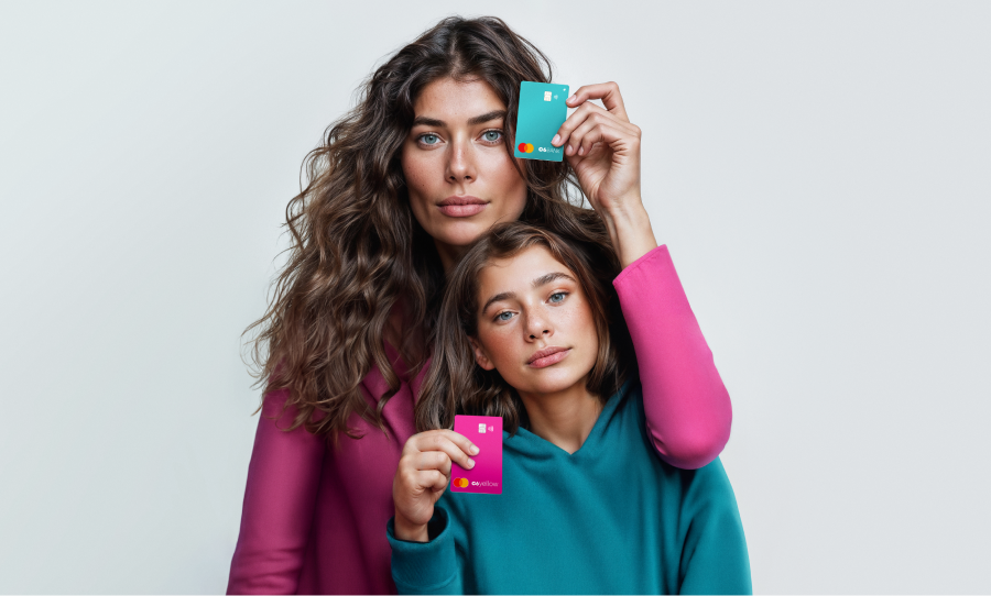 Duas mulheres seguram cartões C6 Bank Acqua e Bubblegum contra um fundo claro.