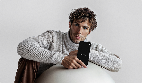 Homem de suéter segura um celular com o app C6 Bank.