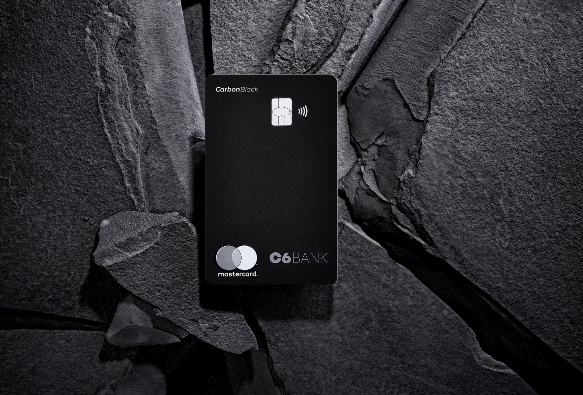 Cartão C6 Carbon Mastercard Black sobre pedra escura, destacando sua textura sofisticada.