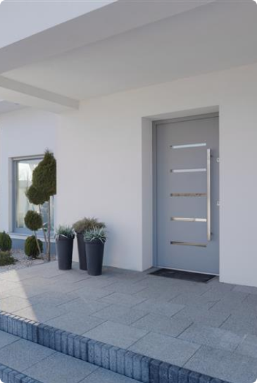Fachada de casa moderna com porta cinza e vasos de plantas.