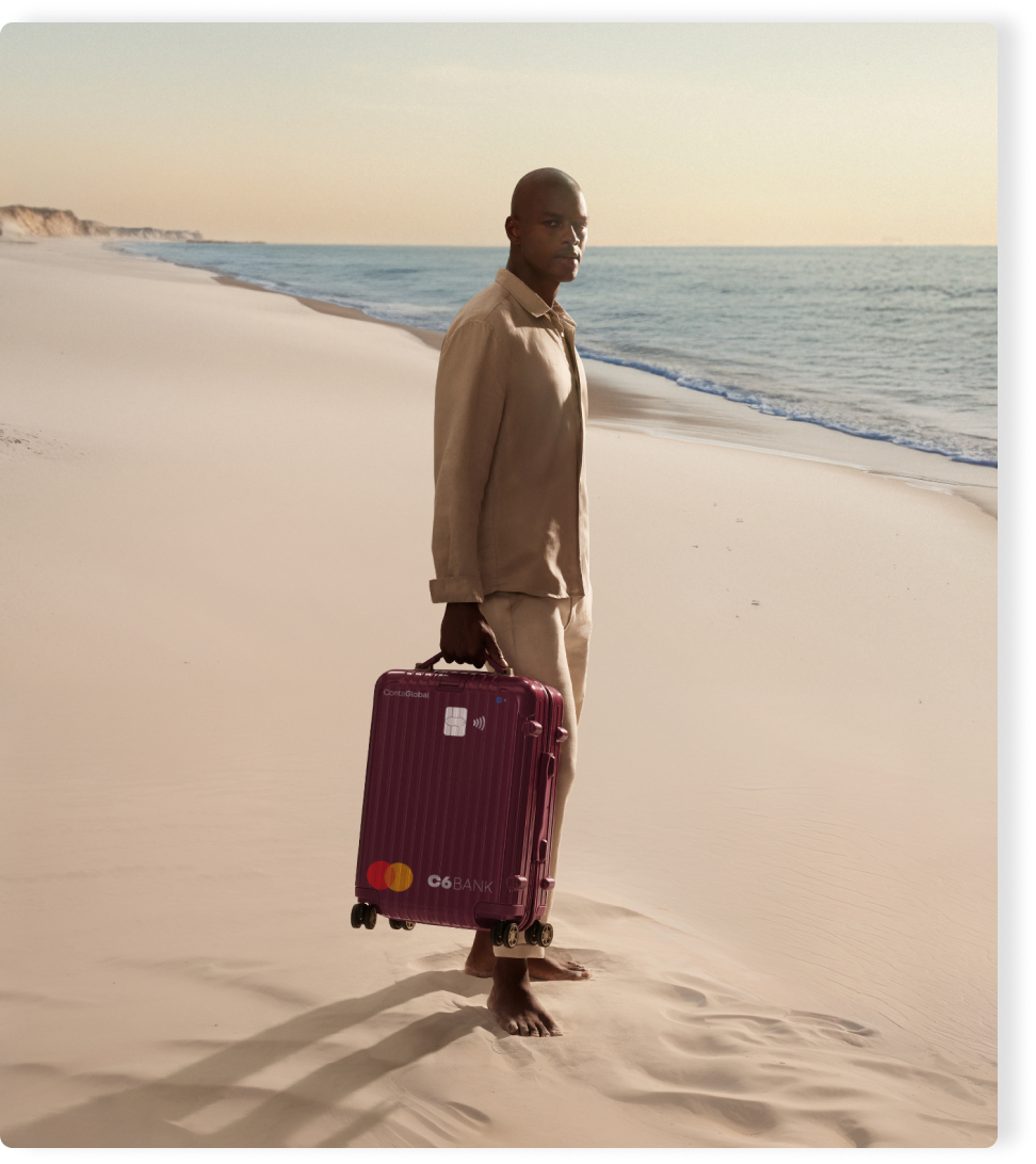 Homem na praia puxa mala com layout do C6 Conta Global. Cena ao entardecer transmite mobilidade e tranquilidade.