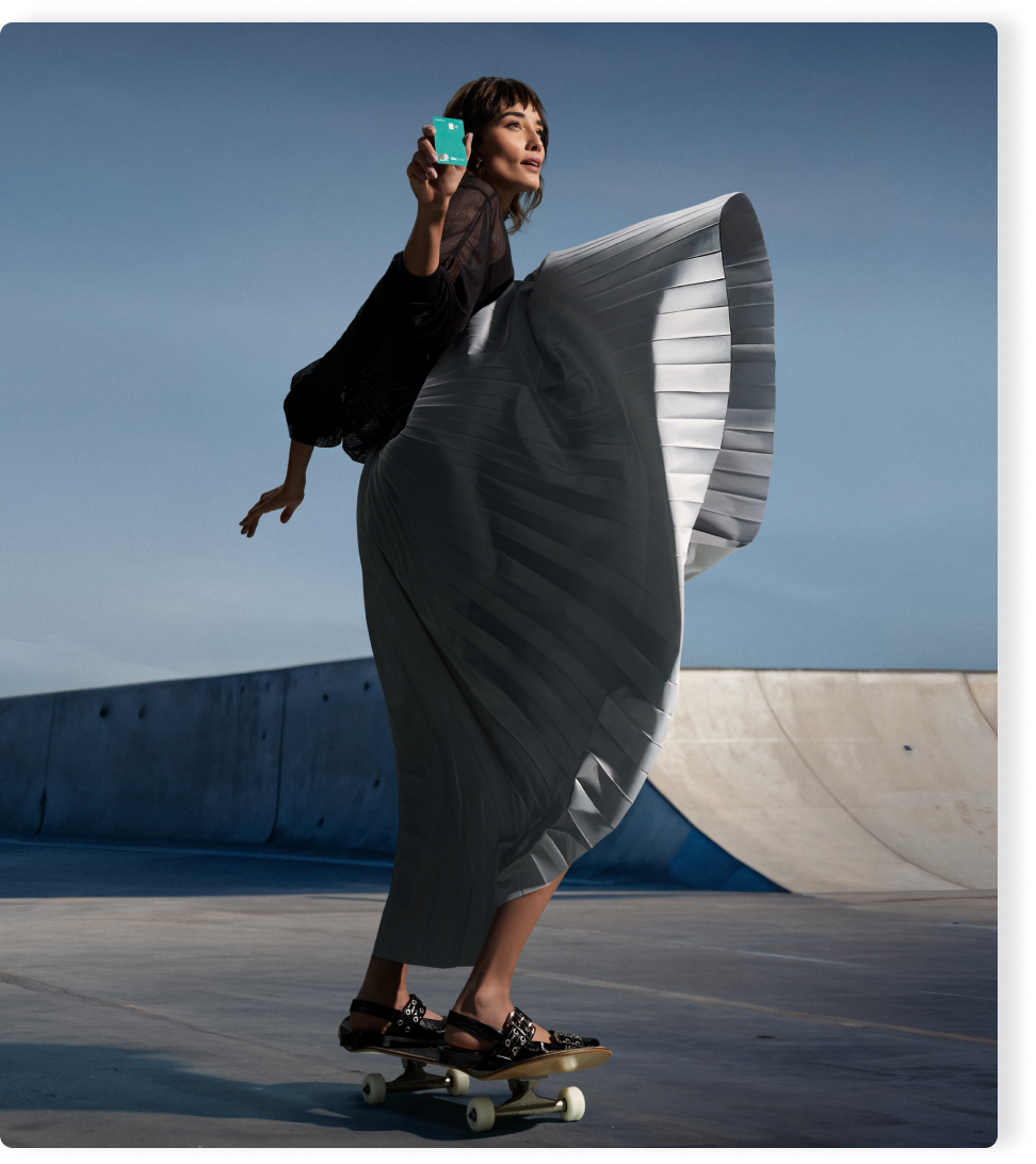 Mulher de skate segura Cartão C6 Acqua com o braço erguido. Cena ao ar livre transmite leveza e liberdade.