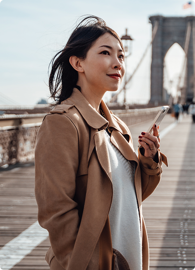 Mulher segura celular na ponte do Brooklyn, com olhar tranquilo para o horizonte.