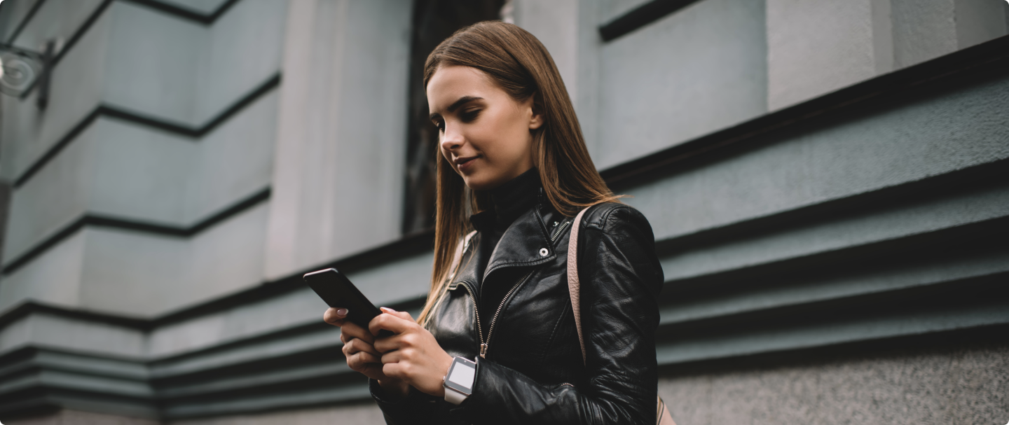 Mulher de cabelos castanhos claros de pé, segurando um celular