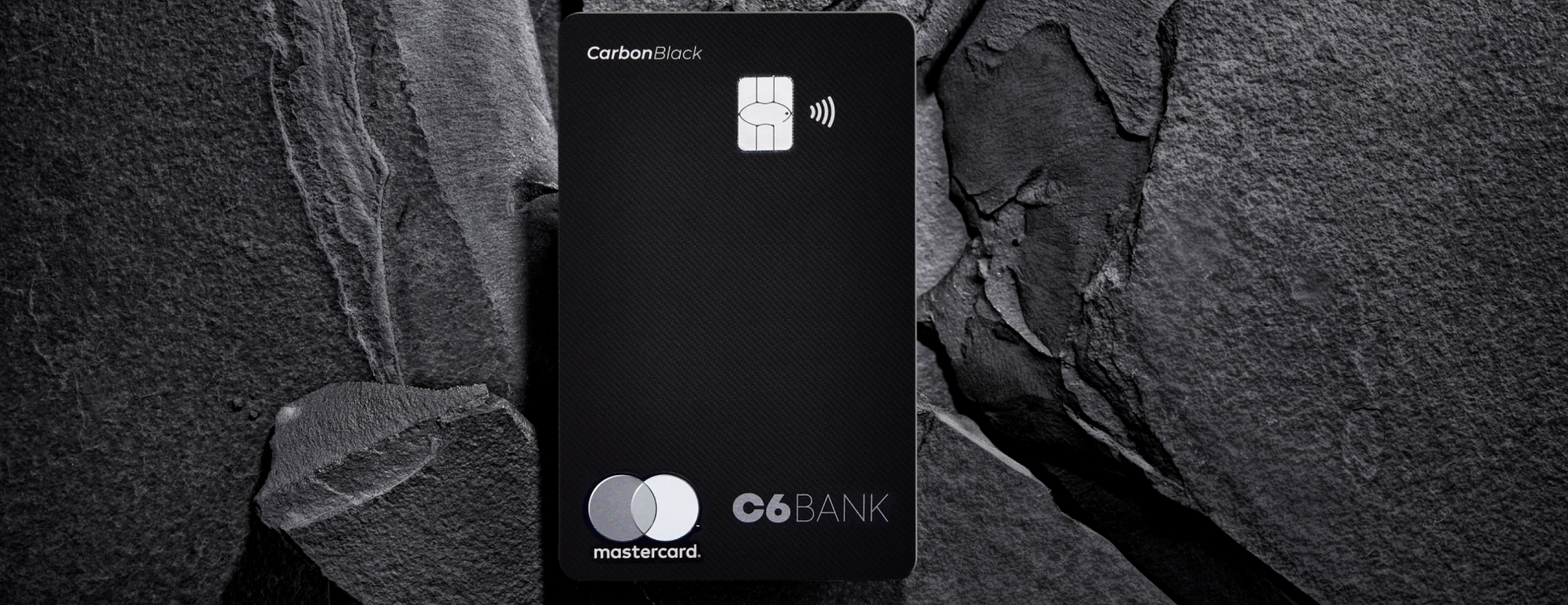 Cartão de crédito C6 Carbon Mastercard Black em cima de fundo de pedras cinzas