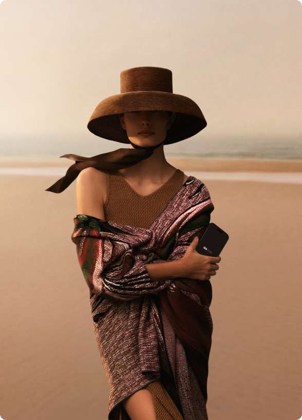Mulher posa em praia segurando um celular com o aplicativo do C6 Bank, com o mar ao fundo.