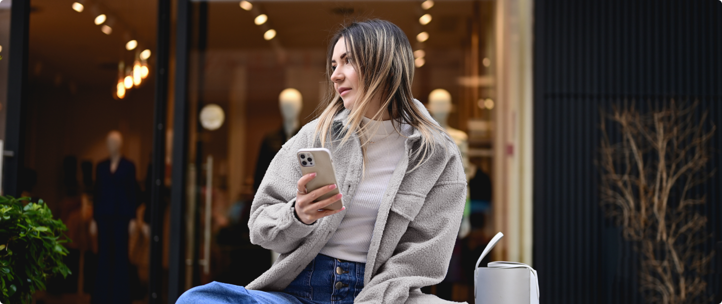 Imagem de mulher de cabelo loiro, sentada segurando seu celular