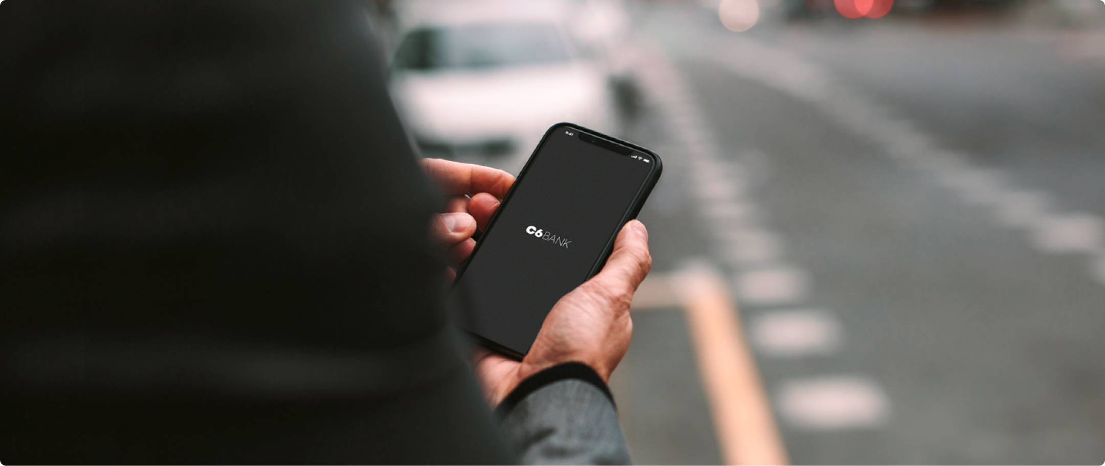 Seguro Celular C6 Bank Fotografia de mão masculina segurando um celular com o logo do C6 Bank com a mão direita
