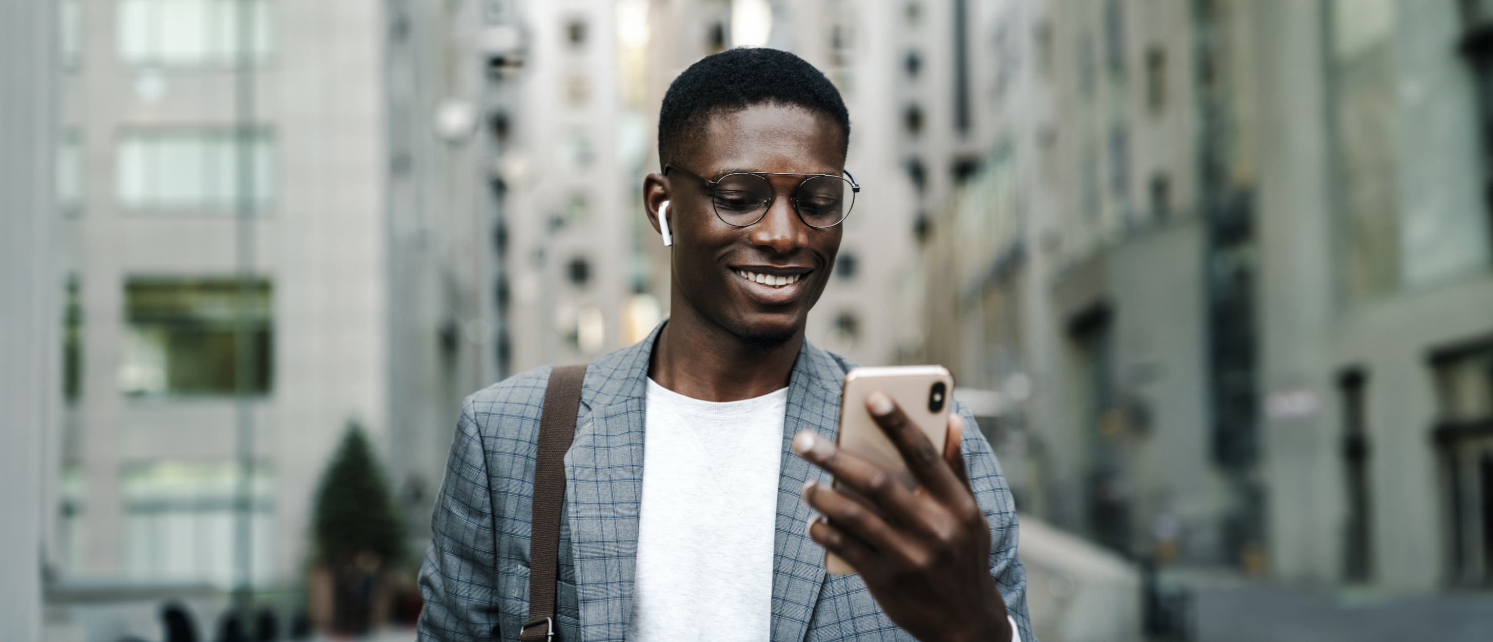 Homem negro de blazer cinza com camiseta branca olhando para o celular em sua mão esquerda