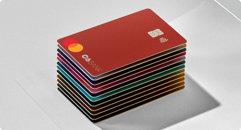 Cartões do C6 Bank empilhados sobre superfície branca com o cartão vermelho no topo em destaque.