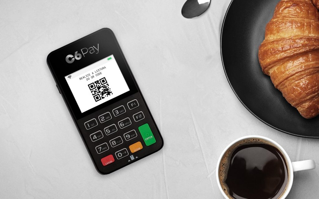 Maquininha C6 Pay ao lado de um café e um croissant