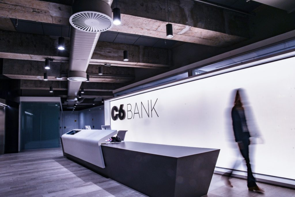 Recepção do prédio do C6 Bank e colaborador andando por uma área comum do banco