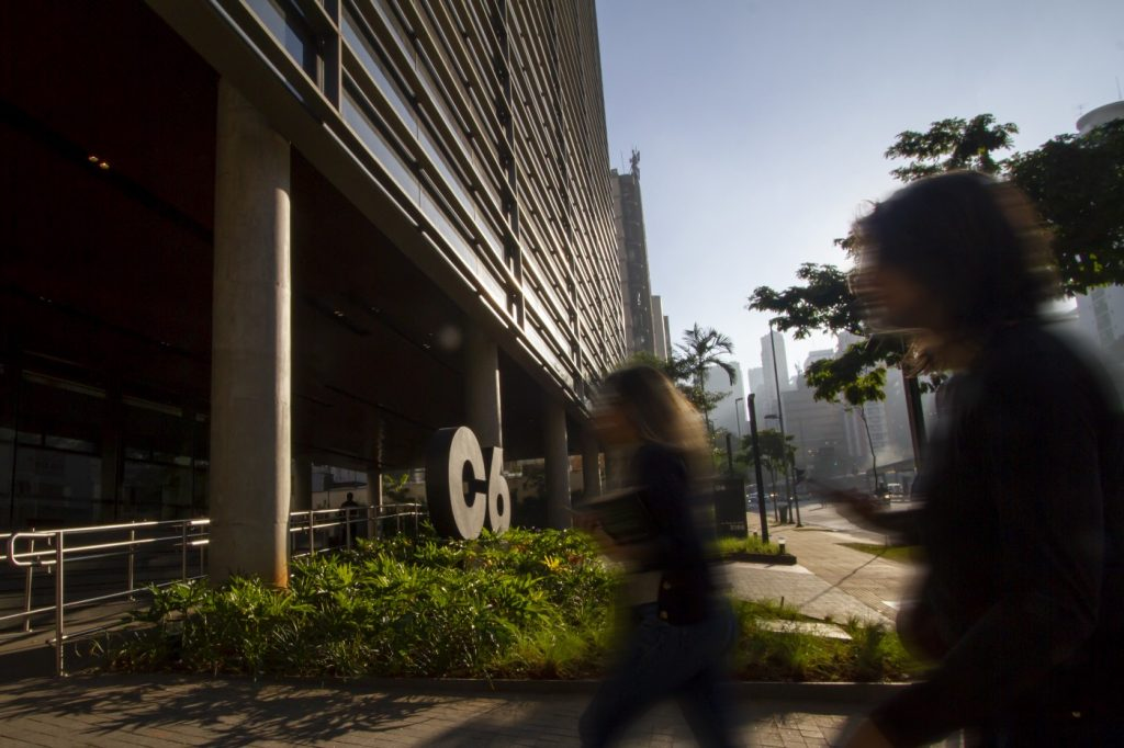 Imagem da fachada do C6 Bank com o vulto de duas pessoas passando