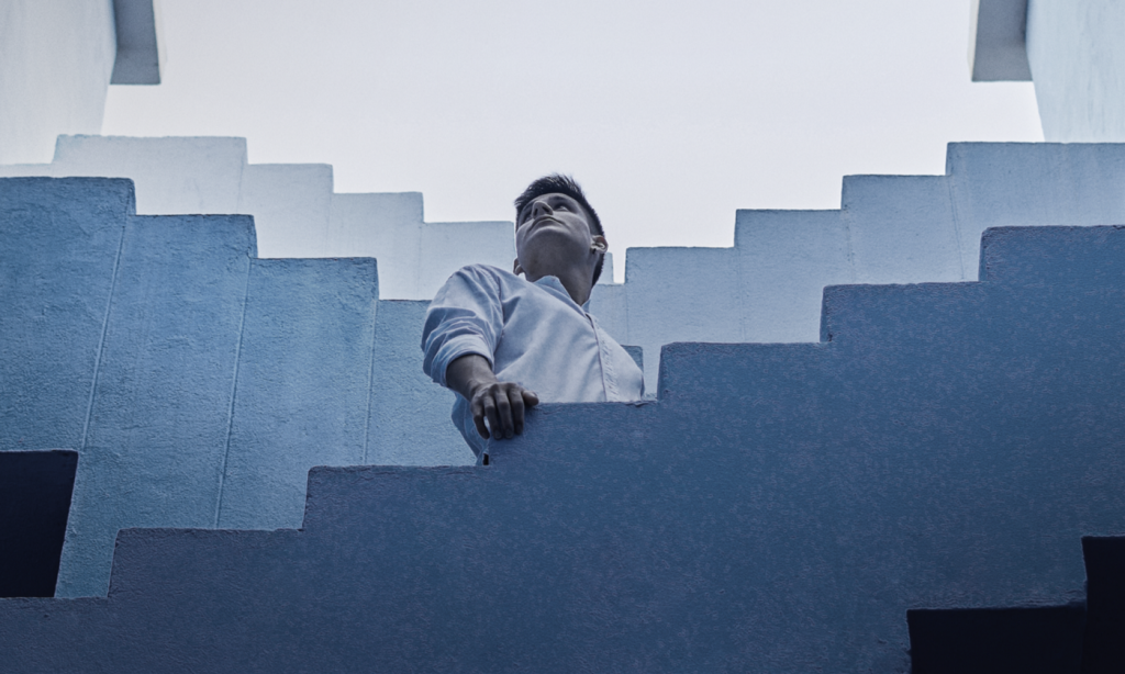 Imagem em tons de azul com homem olhando para cima em veio a degraus de escada