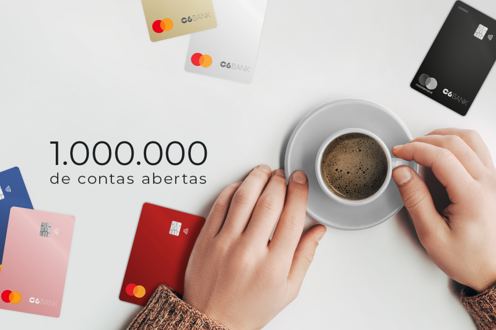 Imagem é foto de cima de uma pessoa segurando uma xícara de café em uma mesa com cartões coloridos do C6 Bank. Do lado esquerdo esrá a frase &quot;1.000.000 de contas abertas&quot;