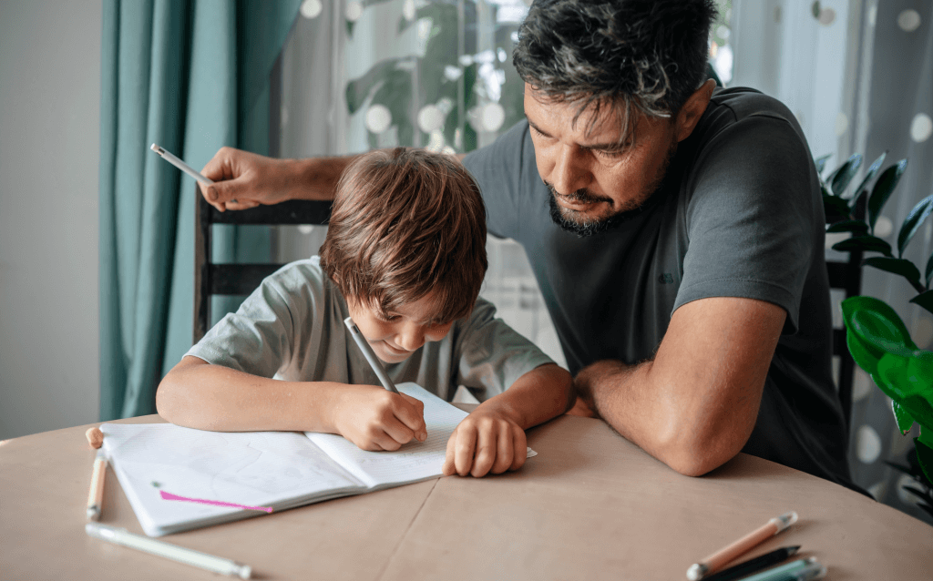 Um pai e seu filho pequeno escrevendo juntos em uma mesa, promovendo a conexão familiar e o aprendizado. Ideal para atividades educativas em casa.