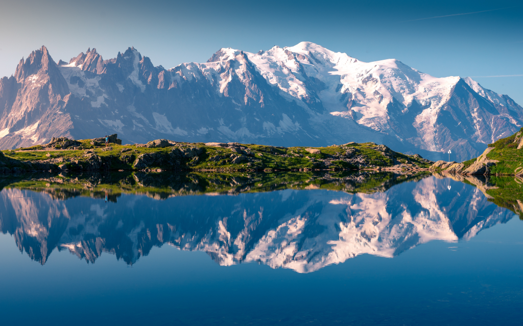 Uma vista deslumbrante das montanhas refletidas em um lago cristalino, com picos cobertos de neve sob um céu claro e azul, ideal para amantes da natureza.