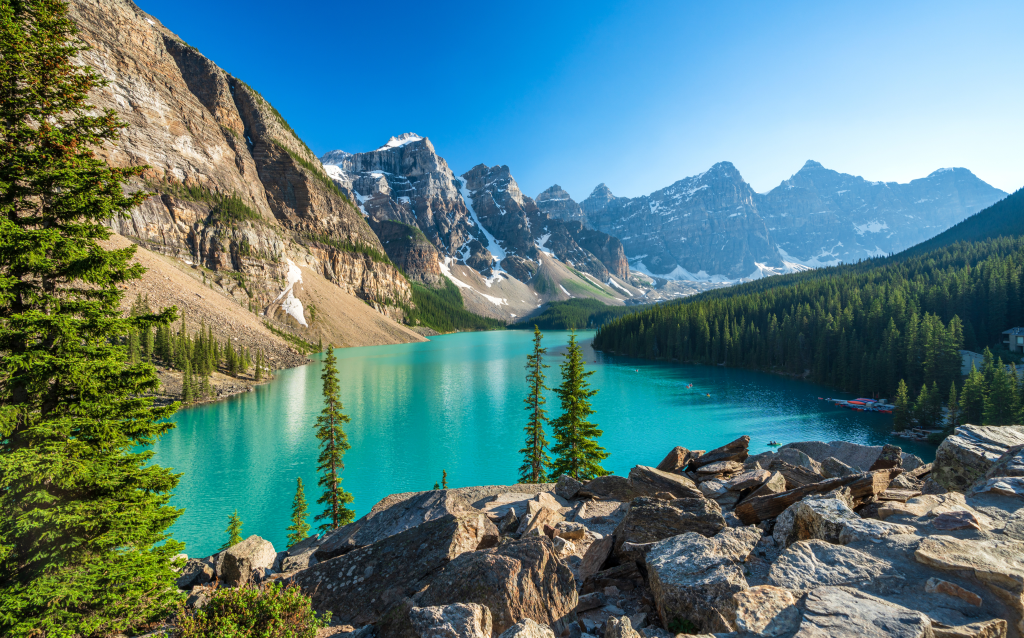 Uma vista impressionante do Lago Moraine, no Canadá, cercado por montanhas majestosas e uma vegetação exuberante, refletindo o céu azul.