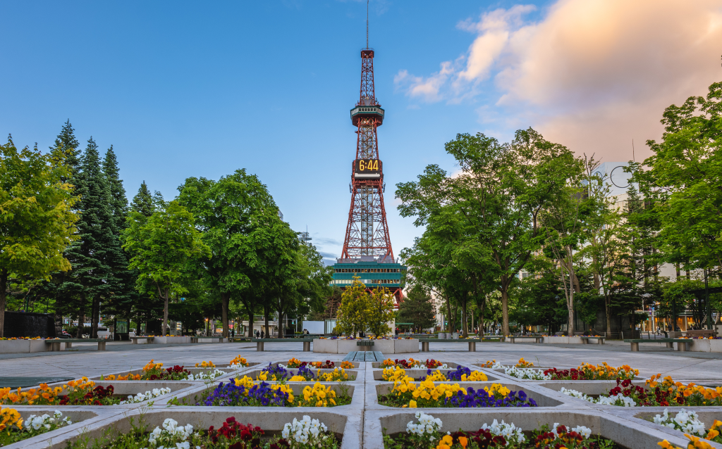 Imagem do Sapporo TV Tower cercada por um belo jardim de flores em Sapporo, Japão. A torre é um marco icônico da cidade.