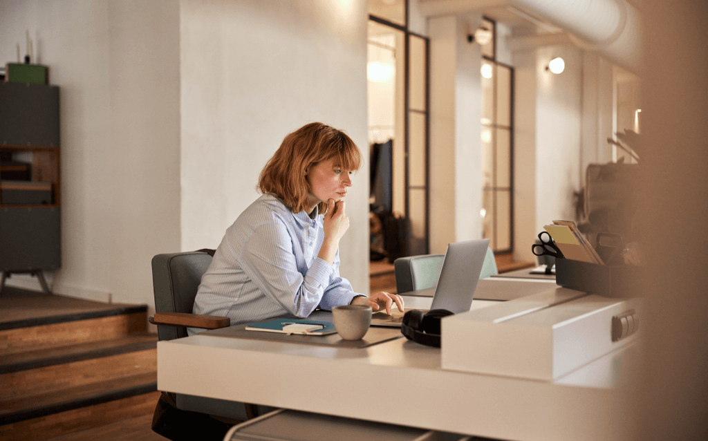 Mulher trabalhando em um ambiente de escritório moderno, concentrada em seu computador portátil, com uma xícara ao lado, inspirando produtividade e dedicação.