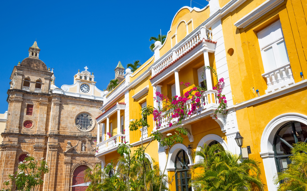 Vista colorida de edifícios históricos em Cartagena, com flores nas varandas e céu azul. A cidade é famosa por sua arquitetura colonial e cultura vibrante.